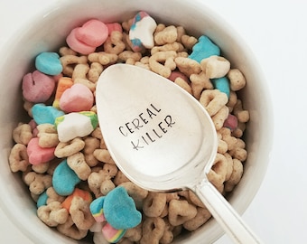 May include: A silver spoon with the words "Cereal Killer" engraved on it, resting in a bowl of colorful cereal.