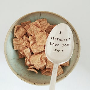 K&ouml;nnte beinhalten: Ein silberner L&ouml;ffel mit der Gravur "I Cerealsly Love You J&hearts;T". Der L&ouml;ffel liegt in einer Sch&uuml;ssel mit M&uuml;sli.