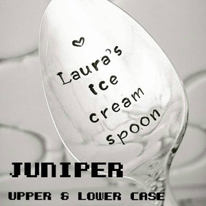 May include: A silver ice cream spoon with the text "Laura's ice cream spoon" and a small heart. The word "JUNIPER" is printed in a pixelated font, with "UPPER & LOWER CASE" below it.