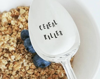 May include: A silver spoon with the text "Cereal Killer" engraved on the front. The spoon is resting in a bowl of cereal and blueberries.