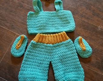 May include: A turquoise crochet baby outfit, including a top, pants, headband, and booties. The pants and booties have a gold-colored trim. The outfit is handmade and designed for a baby.