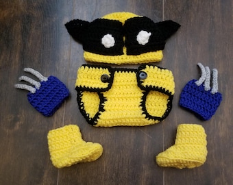 May include: A crocheted baby costume set featuring a yellow and black hat, diaper cover, and booties. The hat has a black mask and white eyes. The booties have a yellow and black color scheme. The set is perfect for a baby's first Halloween costume.