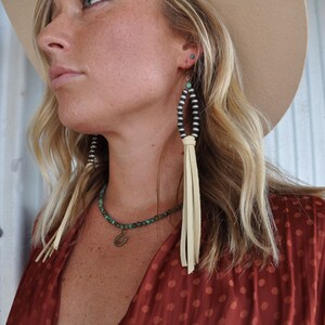 May include: A woman wearing a red polka dot blouse with a turquoise and silver beaded necklace and matching earrings with leather tassels.