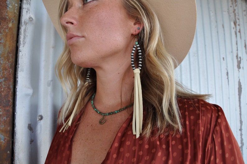 May include: A woman wearing a red polka dot blouse with a turquoise and silver beaded necklace and matching earrings with leather tassels.