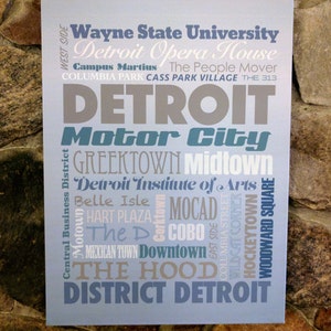 Może przedstawiać: Niebiesko-szary wydruk typograficzny ze słowem "DETROIT" w dużych, pogrubionych literach. Wydruk zawiera listę dzielnic Detroit, zabytków i instytucji kulturalnych, w tym Motor City, Greektown, Midtown, Belle Isle i Detroit Institute of Arts.
