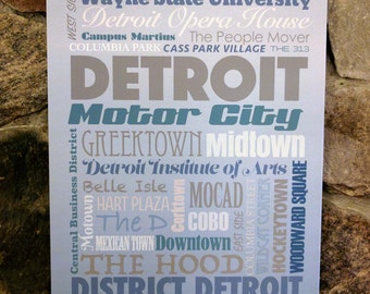 May include: A blue and gray typography print with the word "DETROIT" in large, bold letters. The print features a list of Detroit neighborhoods, landmarks, and cultural institutions, including Motor City, Greektown, Midtown, Belle Isle, and the Detroit Institute of Arts.