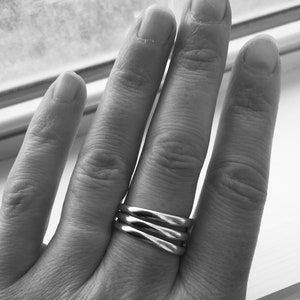 May include: A silver ring with three bands twisted together. The ring is worn on the ring finger of a hand.