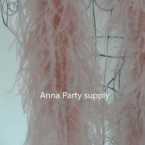Pode incluir: Um boa de penas rosa drapeado sobre um manequim de arame branco. O boa é macio e felpudo, e as penas são longas e esvoaçantes. O texto "Anna Party supply" é visível na imagem.