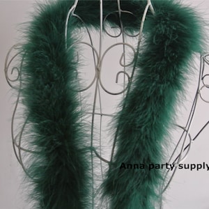 May include: A long, dark green feather boa draped over a white metal display stand. The boa is soft and fluffy, and it would be perfect for adding a touch of glamour to any outfit.