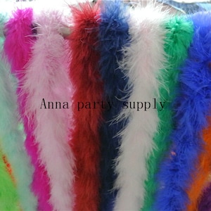 May include: Assortment of feather boas in various colours, including green, light blue, pink, white, red, dark blue, white, green, blue, orange, purple, and yellow. The boas are arranged in a row and are all about 1 metre long. "Anna party supply" is printed on the image.
