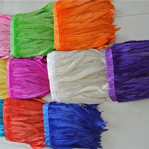 May include: Assortment of feather trim in various colors, including pink, green, orange, white, purple, blue, and red. The trim is made of feathers and has a satin ribbon backing.