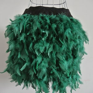Könnte beinhalten: Ein grüner Federrock mit schwarzem Bund. Der Rock besteht aus vielen grünen Federn, die einen vollen, strukturierten Look erzeugen. Der Bund ist schwarz und scheint aus glänzendem Material zu sein.
