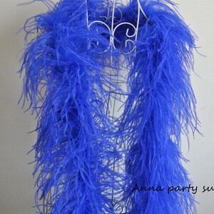 Pode incluir: Uma boa longa de penas de avestruz azul. A boa está drapeada sobre um suporte de metal branco. A boa mede aproximadamente 2 metros de comprimento.