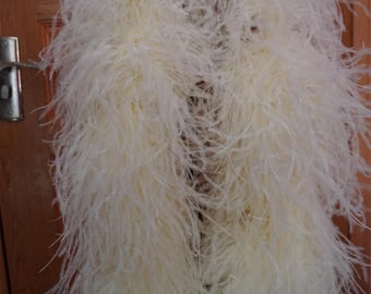 May include: A long, white ostrich feather boa. The boa is draped over a hanger and is shown against a wooden door. The boa is soft and fluffy and would be perfect for a costume or party.