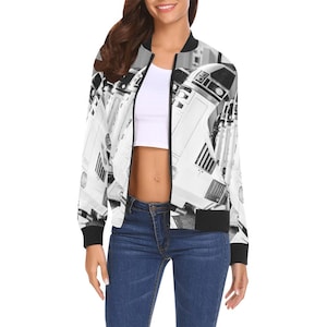 May include: A black and white bomber jacket featuring a repeating pattern of a robot design. The jacket has a black collar, cuffs, and hem. The jacket is open, revealing a white top and blue jeans.