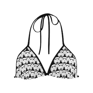 May include: A black and white bikini top featuring a repeating pattern of Stormtrooper helmets. The top has black ties at the neck and back, and a ruffled edge along the bottom. The design is a nod to the Star Wars franchise.