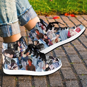 May include: High-top sneakers featuring a collage of faces in various colors and styles. The shoes have black laces, a white sole, and a black trim. The sneakers are worn by a person wearing blue jeans.