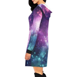 Puede incluir: Vestido con capucha con un estampado de galaxia vibrante en tonos morado, azul y rosa. El vestido tiene mangas largas con pu&ntilde;os negros y una capucha forrada en blanco. El dise&ntilde;o se asemeja a una nebulosa c&oacute;smica.
