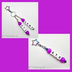 May include: A keychain with a star-shaped charm and two beaded strands. One strand spells "BTS" and the other "ARMY" using white letter beads and purple beads. The star charm has a rainbow iridescent finish.