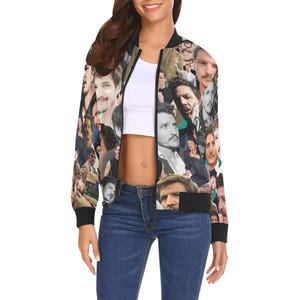 Op de afbeelding: Zwarte bomberjack met een collage van gezichten in verschillende poses. De jas heeft zwarte manchetten, een zwarte kraag en een zwarte zoom. De achtergrond is een mix van zwart, wit en grijstinten.