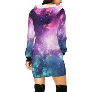 Puede incluir: Vestido con capucha con un vibrante estampado de galaxia en tonos morados, rosas y azules. El vestido de manga larga presenta un forro de capucha blanco y pu&ntilde;os negros. El vestido llega a la rodilla.