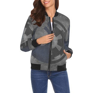 May include: A gray and blue bomber jacket with a geometric design. The jacket has a black collar, cuffs, and hem, and a full-length zipper. The jacket is worn with blue jeans.