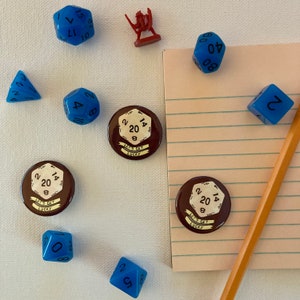 May include: A set of six blue dice with white numbers, two brown circular buttons with white numbers and the text "Let's Get Lucky", and a small red plastic figurine of a knight. The buttons are on a white surface.