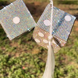 K&ouml;nnte beinhalten: Paar glitzernde W&uuml;rfel-Autozubeh&ouml;rteile, jeweils mit schillernden Strasssteinen bedeckt. Die W&uuml;rfel h&auml;ngen an einer silbernen Kette mit einem wei&szlig;en Quastenanh&auml;nger. Die W&uuml;rfel zeigen die Zahlen eins und f&uuml;nf mit wei&szlig;en Punkten.