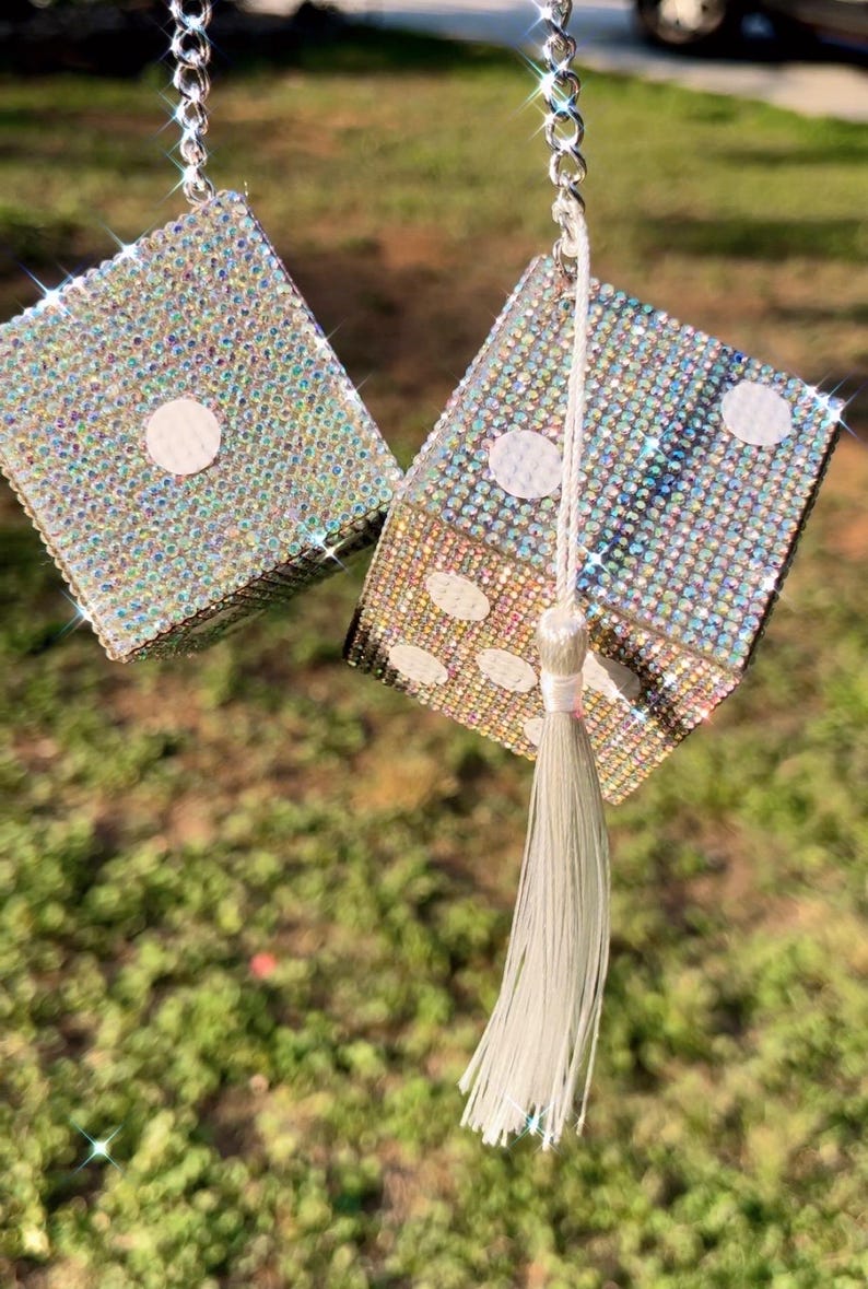 K&ouml;nnte beinhalten: Paar glitzernde W&uuml;rfel-Autozubeh&ouml;rteile, jeweils mit schillernden Strasssteinen bedeckt. Die W&uuml;rfel h&auml;ngen an einer silbernen Kette mit einem wei&szlig;en Quastenanh&auml;nger. Die W&uuml;rfel zeigen die Zahlen eins und f&uuml;nf mit wei&szlig;en Punkten.