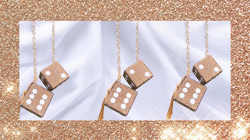 K&ouml;nnte beinhalten: Drei Paare h&auml;ngender W&uuml;rfel, jeweils mit einer goldenen Kette und Quaste. Die W&uuml;rfel sind beige mit wei&szlig;en Punkten. Der Hintergrund ist wei&szlig;er Stoff mit einem goldenen Glitzerrahmen.