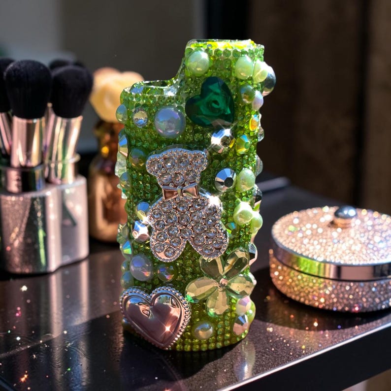 Peut inclure: Un &eacute;tui vert orn&eacute; de bijoux avec un motif d'ours en peluche. L'&eacute;tui est recouvert de perles vertes, de pierres pr&eacute;cieuses transparentes et d'accents argent&eacute;s. Un c&oelig;ur argent&eacute; et un tr&egrave;fle sont &eacute;galement pr&eacute;sents sur l'&eacute;tui. L'&eacute;tui est pos&eacute; sur une surface noire.