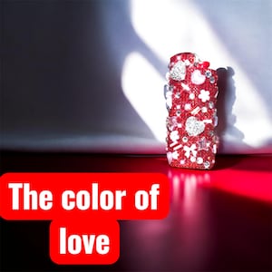 Peut inclure: Un briquet rouge orn&eacute; de strass, de c&oelig;urs et de motifs floraux. Le briquet a un petit n&oelig;ud rouge et le texte "The color of love" dans un rectangle rouge.