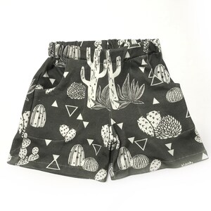 May include: Dark gray shorts with a white cactus print. The shorts have pockets and a drawstring waist.