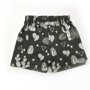 May include: Black shorts with a white cactus print. The shorts have an elastic waistband and a drawstring.
