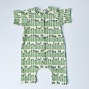 May include: A white baby onesie with a green asparagus print. The onesie has short sleeves and a button closure.
