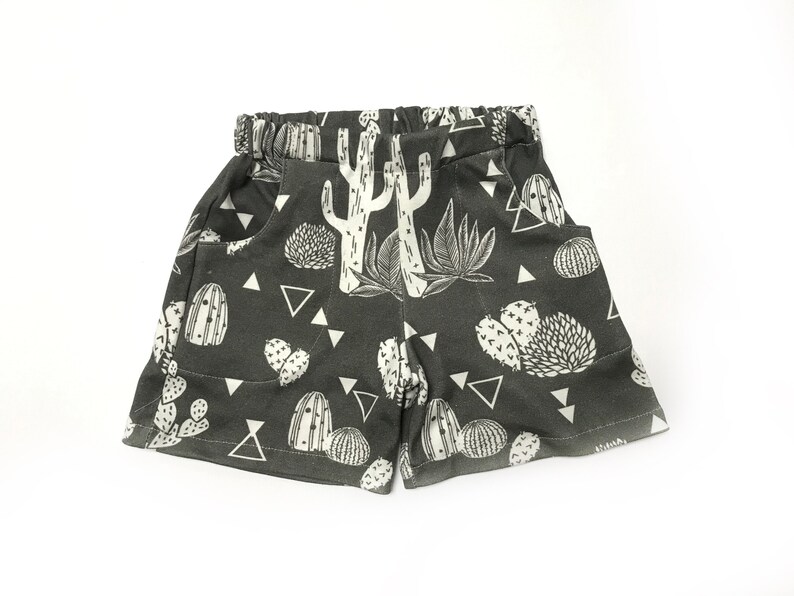 May include: Dark gray shorts with a white cactus print. The shorts have pockets and a drawstring waist.