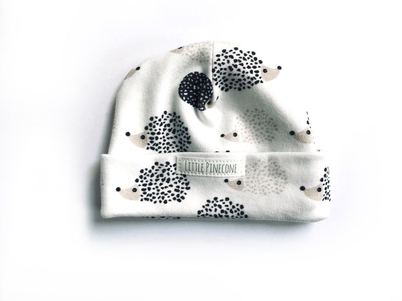 May include: White baby hat with a hedgehog print and a small label that says "Little Pinecone".