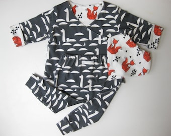 May include: A gray pajama set with a llama and half-moon pattern. The top has a wrap-around design with red fox accents. The matching pants and a small square item complete the set. The set is made of soft fabric.