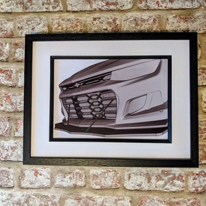 May include: A black and white photo of the front of a car, showing the grill and headlights. The car is framed in a black frame.