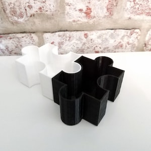 May include: A white and black puzzle-shaped desktop organizer with two compartments.