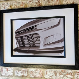 May include: A black and white photo of the front of a silver car. The car has a black grille and a black bumper. The photo is framed in a black frame.