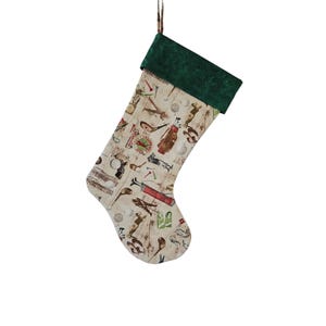 May include: A Christmas stocking with a golf theme. The stocking has a cream-colored background with golf-related illustrations, including golf clubs, golf balls, and golf bags. The cuff is a dark green velvet material, and a green and brown ribbon is attached for hanging.