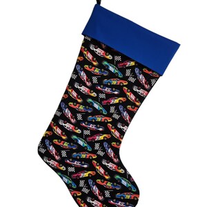 May include: A Christmas stocking with a black background and a blue cuff. The stocking is decorated with a pattern of colorful race cars and checkered flags.