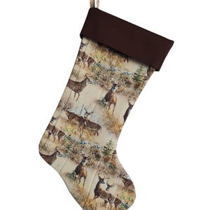 May include: A brown and beige Christmas stocking with a brown cuff. The stocking is decorated with a pattern of white-tailed deer in a woodland setting.