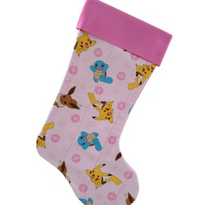 May include: Pink Christmas stocking with a quilted design featuring various Pokemon characters, including Pikachu, Squirtle, and Eevee. The stocking has a pink cuff.