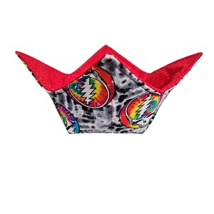 May include: A fabric bowl cozy with a red interior and exterior trim. The exterior features a pattern of tie-dye skulls on a gray and white leopard print background. The bowl cozy is designed to hold a bowl of hot food.