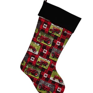 May include: A Christmas stocking with a black cuff and a red and black plaid pattern. The stocking is decorated with images of red tractors and the IH Farm logo. A red loop is attached for hanging.