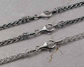 May include: Three silver chains featuring intricate, ornate end caps with lobster claw clasps. Each clasp is stamped with 925, indicating sterling silver. The chains have a woven, braided texture and a polished, metallic finish.