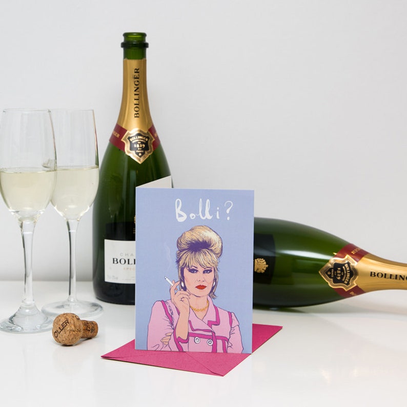 Peut inclure: Une carte de v&oelig;ux avec une illustration de dessin anim&eacute; d'une femme aux cheveux blonds tenant une cigarette. La carte a un fond bleu et le texte "Bolli?" en blanc. Deux bouteilles de champagne et deux verres de champagne sont en arri&egrave;re-plan.