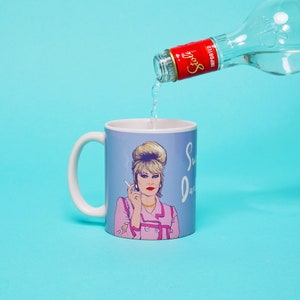 Peut inclure: Une tasse en c&eacute;ramique bleue avec une anse blanche pr&eacute;sente une illustration de dessin anim&eacute; d'une femme aux cheveux blonds fumant une cigarette. La tasse porte l'inscription "Sweet Jane". Une bouteille d'alcool clair est vers&eacute;e dans la tasse.